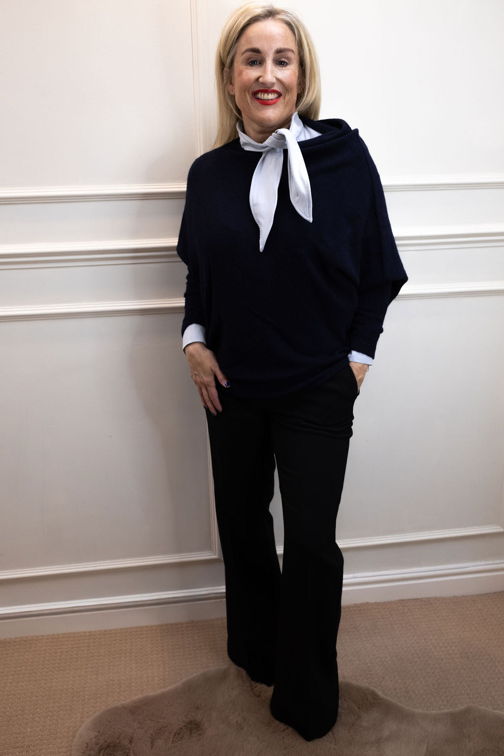 Front view of a woman wearing the light blue Sofia shirt under a navy knit with black wide-leg trousers.