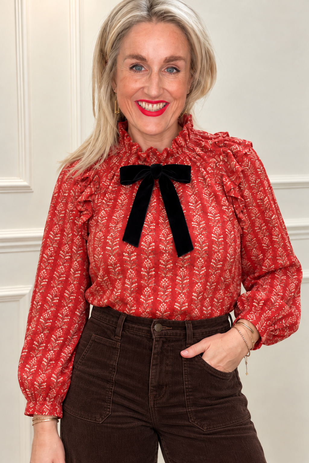 Maison de Belle Nora Tie Neck Blouse in red block print with a black velvet bow and ruffled collar, tucked into dark brown cords