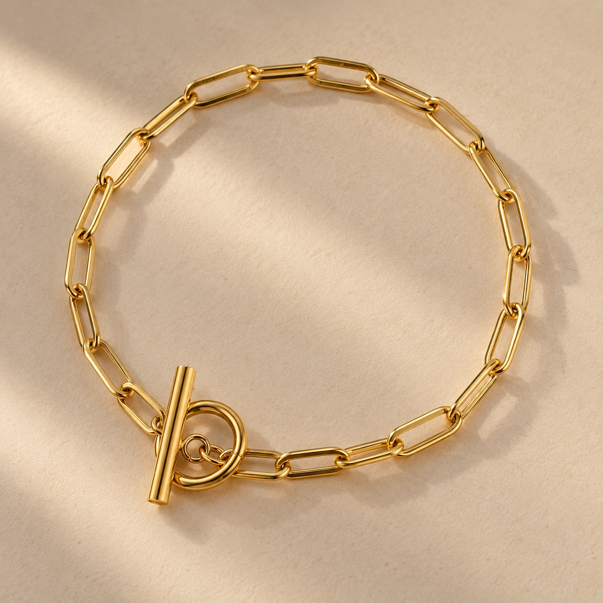 Gold-plated paperclip-link bracelet with a T-bar clasp on a cream surface.