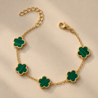 Gold-plated bracelet with five green flower-shaped charms, shown on a cream surface.