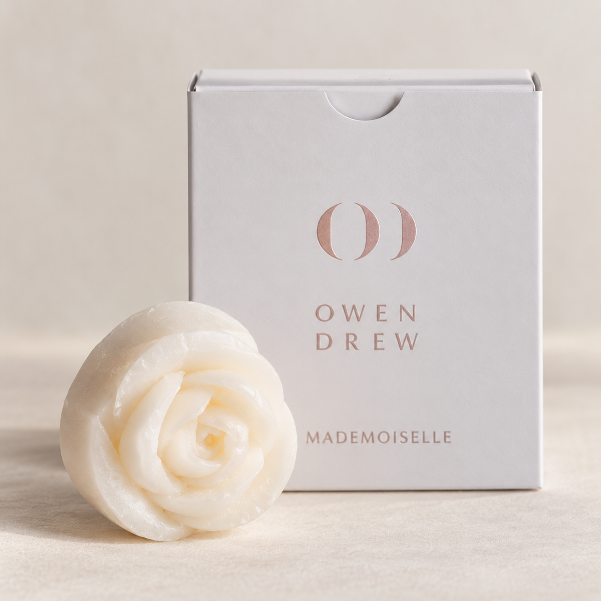 Close-up of white rose-shaped Owen Drew Mademoiselle wax melt in front of its branded box