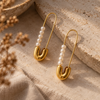 Gold-plated safety-pin shaped earrings with rows of white pearls on a stone slab.