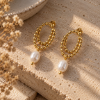 Gold-plated double-loop chain earrings with white pearl drops, arranged on a stone slab.