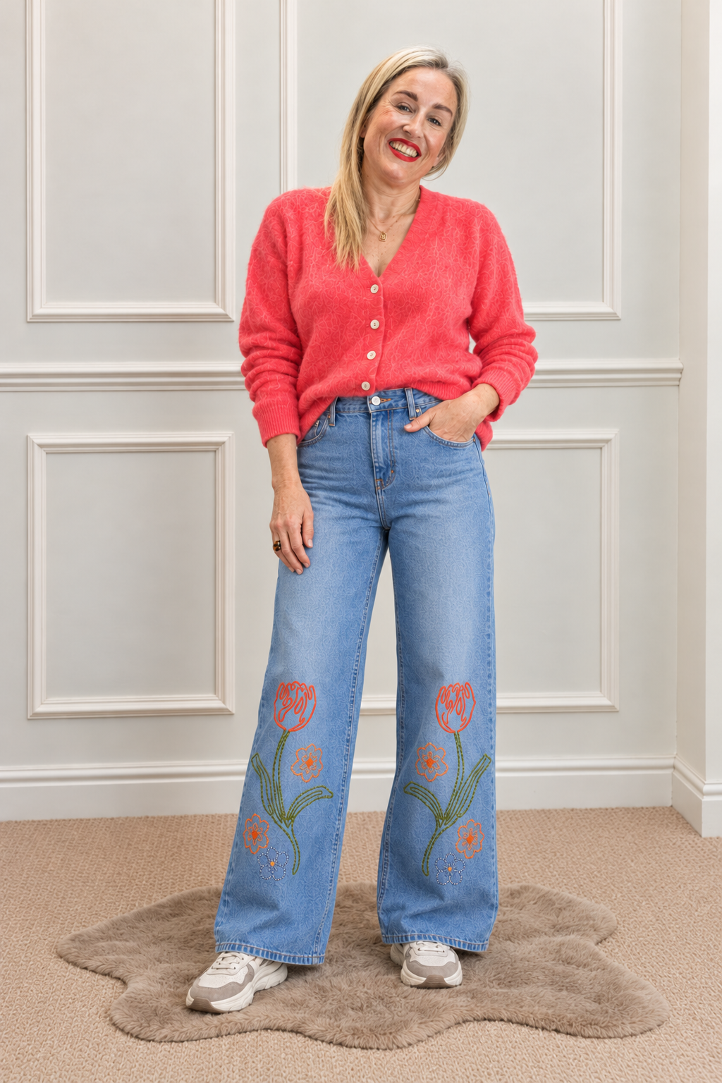 Hester mid-blue wide-leg jeans with orange flowers and green stems, worn with a coral cardigan.
