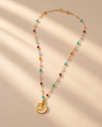 Sorbet necklace with multicoloured beads and round gold-tone pendant on a cream surface.