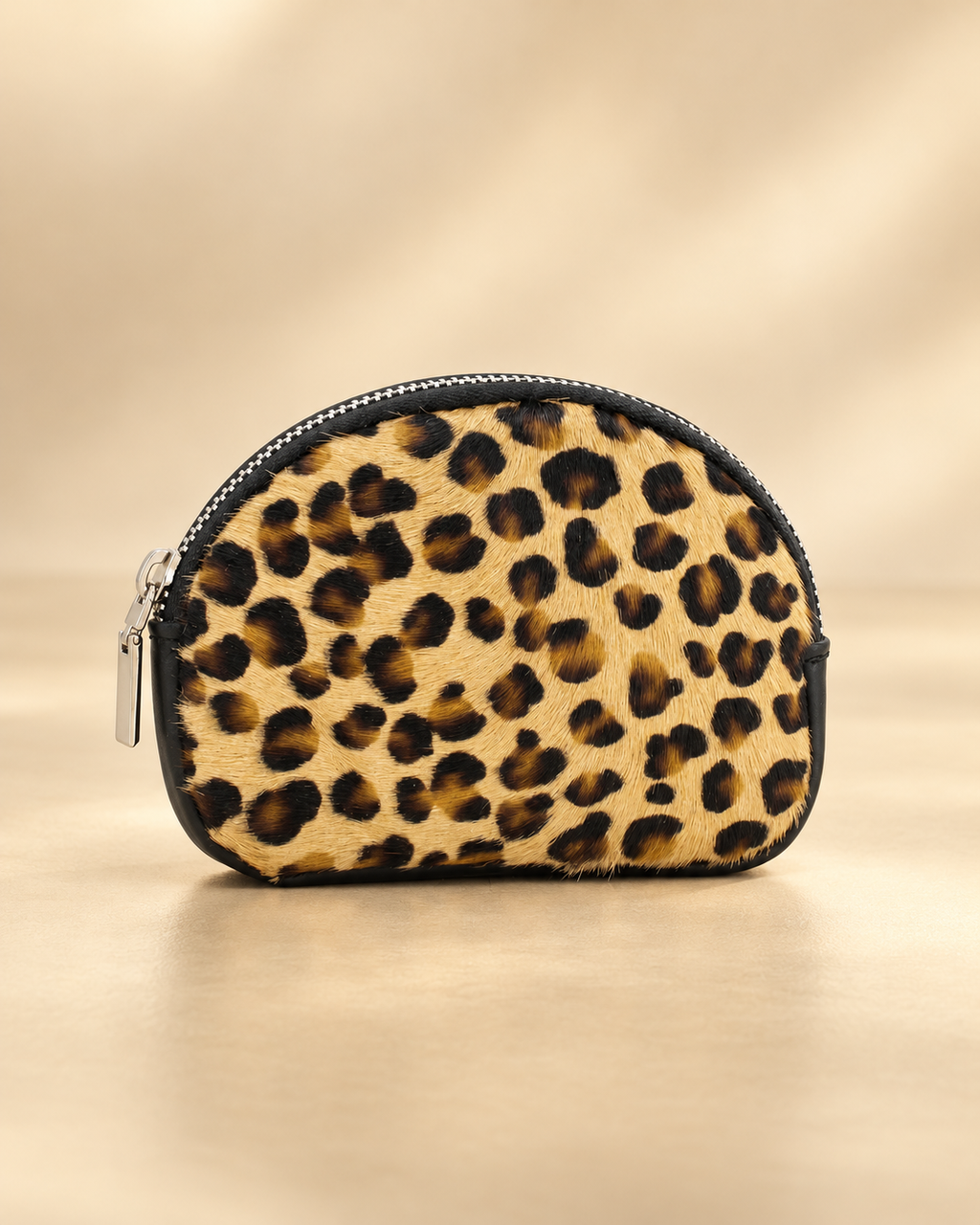 Front-facing studio photograph of Bari small leopard-print leather purse on a light golden backdrop, showing faux pony skin, black trim and silver zip.
