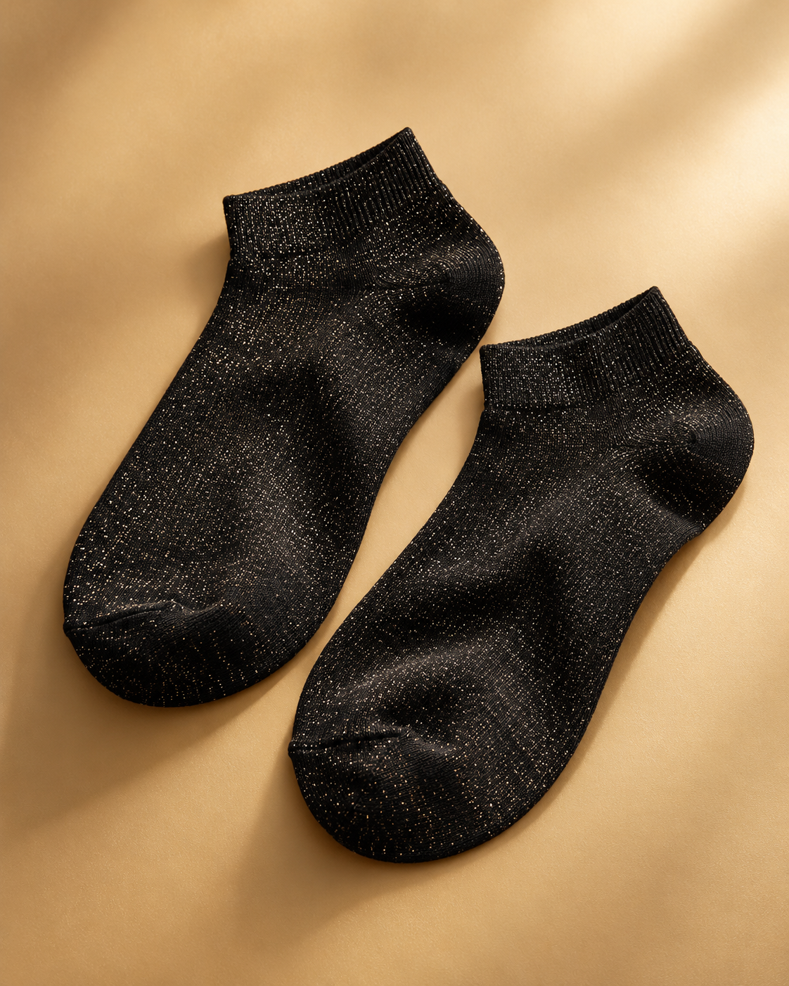 Black glitter sneaker socks in a second flat-lay arrangement on a golden neutral background