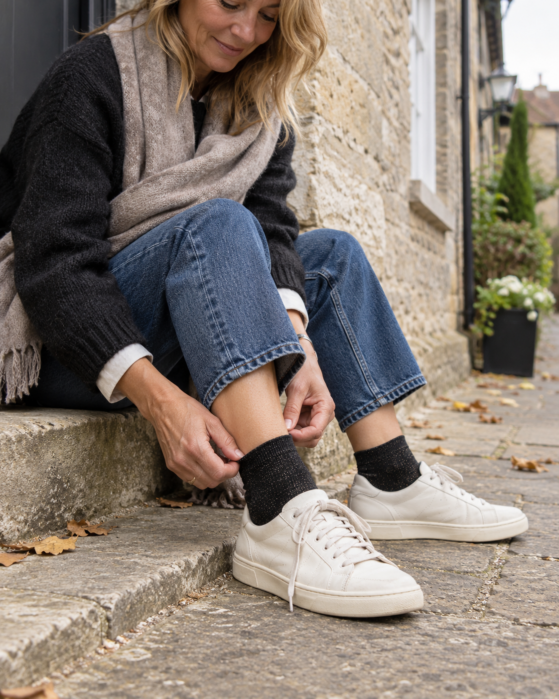 Woman wearing black glitter sneaker socks, cropped blue jeans and white trainers on stone steps
