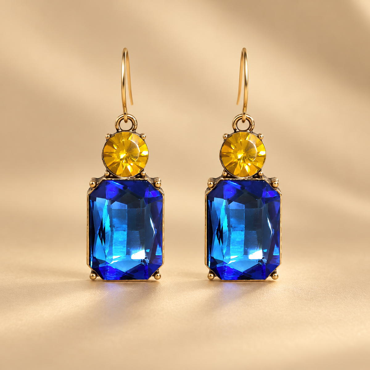 Azure and Yellow Twin Gem earrings on minimal warm golden studio background, gold hooks, round yellow stones and faceted blue gemstone drops
